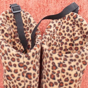 May include: Two brown and tan leopard print fabric pet beds with black straps. The beds are made of soft, plush fabric and have a round shape.