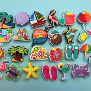 Puede incluir: Una colección de dijes para zapatos con temática veraniega que incluye varios diseños como palmeras, una concha, un velero, un flamenco, un cubo de playa, una pelota, una tortuga marina, un cóctel, chanclas, un cangrejo y un letrero que dice BEACH.