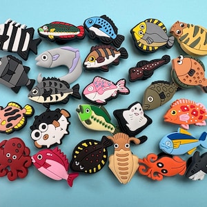 May include: A collection of colourful silicone shoe charms shaped like various sea creatures, including fish, an octopus, a squid, and a shark. The assortment features diverse species in vibrant colours like red, orange, yellow, blue, pink, and black.