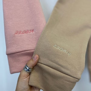 May include: Two sweatshirts, one pink and one beige, with the date "23.08.14" embroidered on the cuffs.