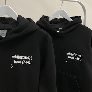 May include: Two black hoodies with white text. The text on the left hoodie reads "while(true){ love (her); }" and the text on the right hoodie reads "while(true) { love (him); }"