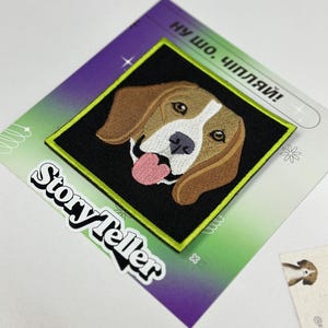 May include: A black and white embroidered patch of a beagle dog with a pink tongue sticking out. The patch is surrounded by a bright green border and the text "Storyteller" is printed in white on a black background. The text "Ну шо, чипляй!" is printed in black on a white background.