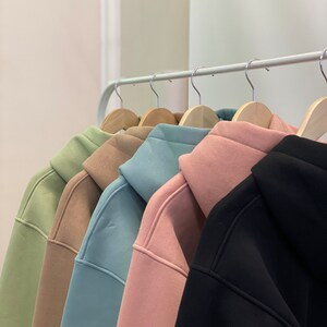 Peut inclure: Cinq sweat-shirts &agrave; capuche suspendus &agrave; un portant. Les sweat-shirts sont de diff&eacute;rentes couleurs&nbsp;: vert, marron, bleu clair, rose et noir.