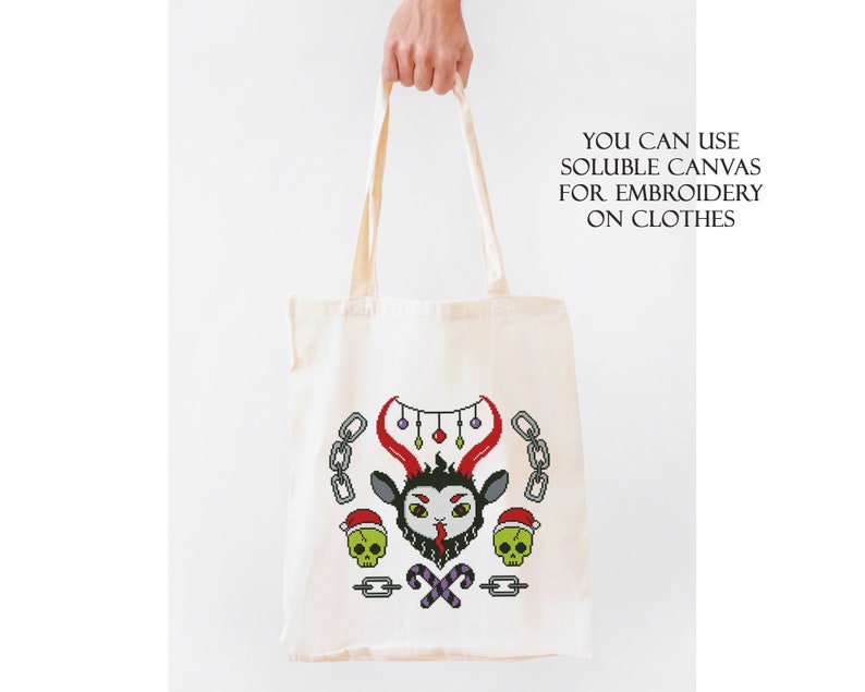 May include: A white tote bag with a black and red embroidered design of a goat head with horns, candy canes, and skulls. The text "YOU CAN USE SOLUBLE CANVAS FOR EMBROIDERY ON CLOTHES" is printed on the bag.