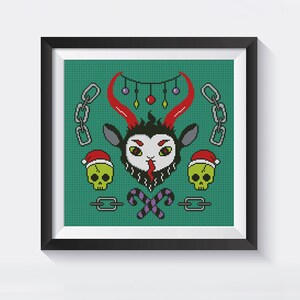 May include: A framed cross-stitch design featuring a green background with a black and red goat head with horns, two green skulls with red Santa hats, candy canes, and chains. The design has a festive, Christmas theme.
