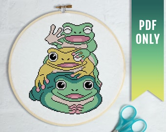 May include: Cross stitch pattern of three green frogs stacked on top of each other. The bottom frog is green with a pink mouth, the middle frog is yellow with a pink mouth, and the top frog is green with a pink mouth. The frogs are all smiling.
