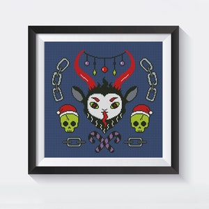 May include: A framed cross-stitch design featuring a cartoon goat with red horns, a black beard, and a tongue sticking out. The goat is wearing a Santa hat and surrounded by Christmas ornaments, candy canes, and chains.