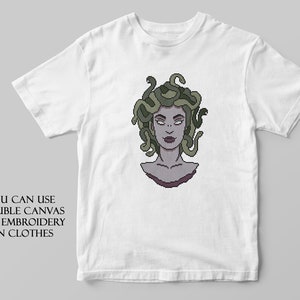 May include: White t-shirt with a pixelated image of Medusa, a mythical Greek figure with snakes for hair. The text "YOU CAN USE SOLUBLE CANVAS FOR EMBROIDERY ON CLOTHES" is printed below the image.
