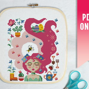 Puede incluir: Bordado de punto de cruz de una mujer con cabello rosa y vestido verde, rodeada de flores, una abeja y herramientas de jardinería. El diseño está enmarcado en un aro de madera. El texto "PDF ONLY" está en el lado derecho.