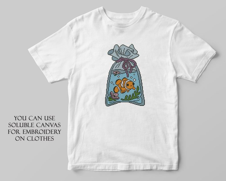 May include: White t-shirt with an embroidered design of a clownfish in a bag of water. The text "YOU CAN USE SOLUBLE CANVAS FOR EMBROIDERY ON CLOTHES" is printed below the design.