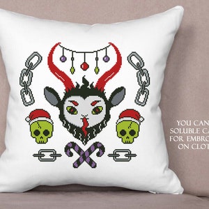 May include: A white pillow with a cross-stitch design featuring a red and black devil with horns, candy canes, skulls, and a chain. The text "YOU CAN USE SOLUBLE CANVAS FOR EMBROIDERY ON CLOTHES" is printed on the pillow.