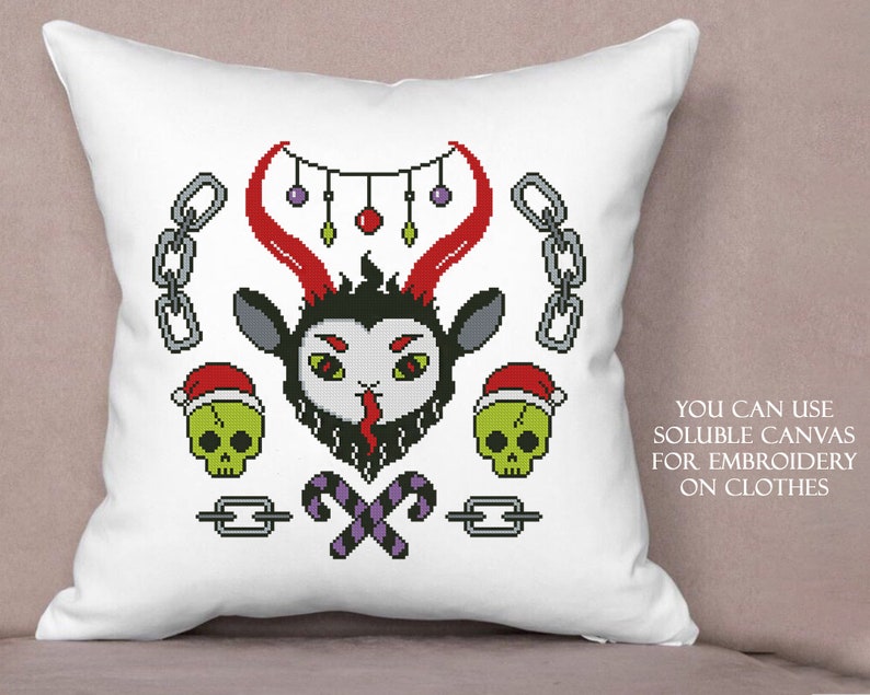 May include: A white pillow with a cross-stitch design featuring a red and black devil with horns, candy canes, skulls, and a chain. The text "YOU CAN USE SOLUBLE CANVAS FOR EMBROIDERY ON CLOTHES" is printed on the pillow.