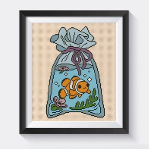 May include: A cross-stitch pattern of an orange and white clownfish swimming in a blue plastic bag with a purple ribbon tied around the top.