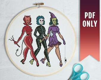 May include: Cross stitch pattern featuring three figures in Halloween costumes: a red devil, a skeleton, and a witch with a purple dress and a spider web. The pattern is displayed on a white background in a circular embroidery hoop.