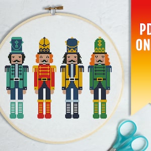 Könnte beinhalten: Kreuzstichmuster mit vier Nussknacker-Soldaten in verschiedenen Farben. Die Nussknacker tragen traditionelle Kostüme mit Hüten und Stiefeln. Das Muster ist für Kreuzstich konzipiert und als PDF-Download erhältlich.