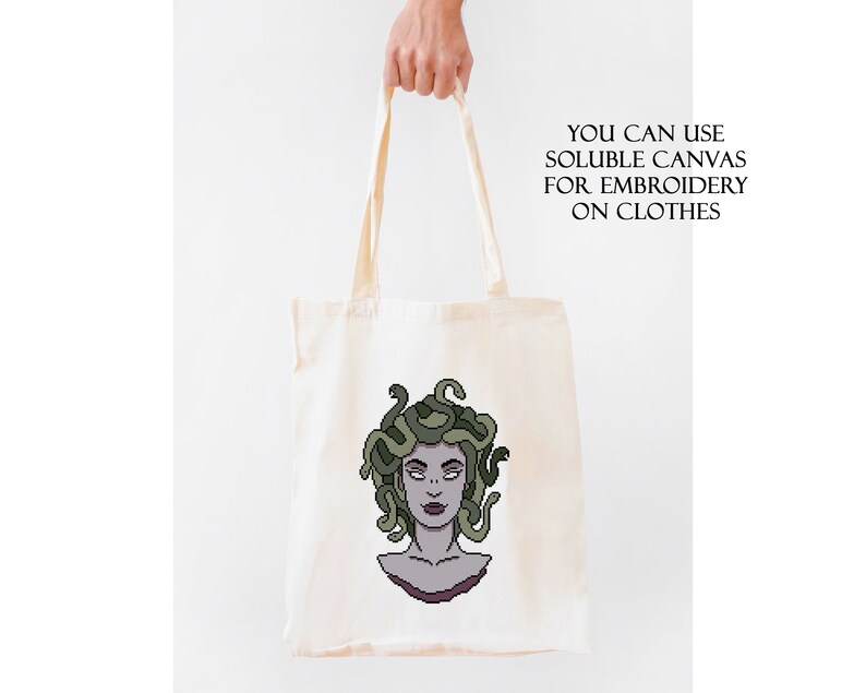 May include: A white tote bag with a green and purple illustration of Medusa, a mythical Greek figure with snakes for hair. The text "YOU CAN USE SOLUBLE CANVAS FOR EMBROIDERY ON CLOTHES" is printed on the bag.