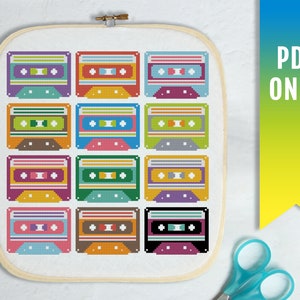 Puede incluir: Un patrón de punto de cruz con 12 cintas de cassette de colores. Las cintas están dispuestas en una cuadrícula y tienen diferentes colores y diseños. El patrón está enmarcado en un marco de madera blanco.