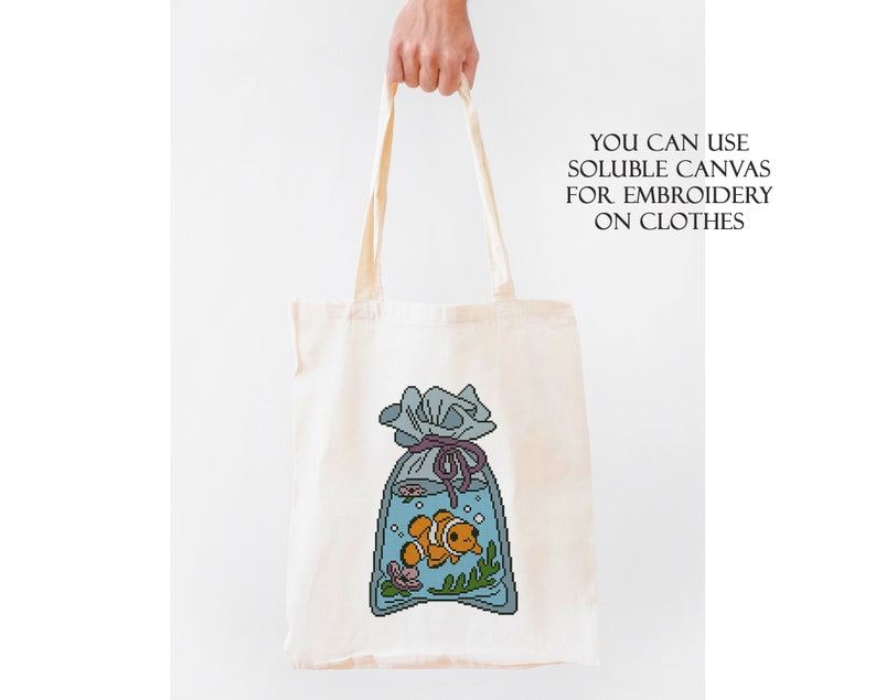 May include: A white tote bag with a blue and orange cartoon fish in a bag with a purple ribbon. The text "YOU CAN USE SOLUBLE CANVAS FOR EMBROIDERY ON CLOTHES" is printed on the bag.