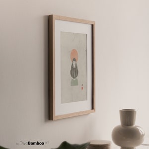 May include: A framed print of a black and white illustration of a monkey sitting on a green platform with a red sun behind it. The print is on a light green background with the Japanese character for "monkey" in red in the bottom right corner.