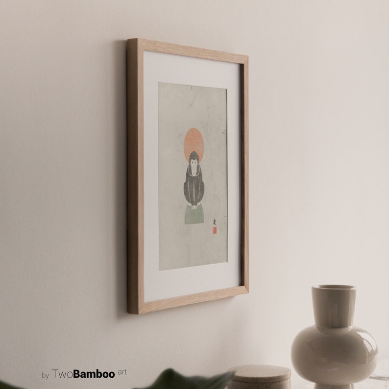 May include: A framed print of a black and white illustration of a monkey sitting on a green platform with a red sun behind it. The print is on a light green background with the Japanese character for "monkey" in red in the bottom right corner.