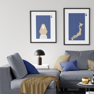 May include: Two framed prints with a blue background and gold accents. The print on the left features a stylized monkey, while the print on the right shows a map of Japan. The prints are hanging on a white wall above a gray couch with blue pillows.
