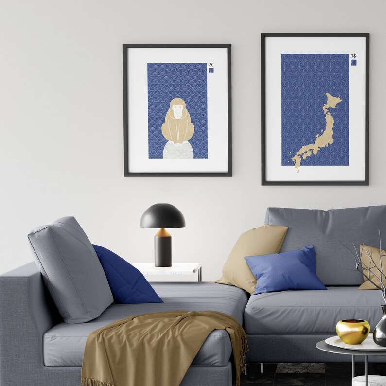 May include: Two framed prints with a blue background and gold accents. The print on the left features a stylized monkey, while the print on the right shows a map of Japan. The prints are hanging on a white wall above a gray couch with blue pillows.