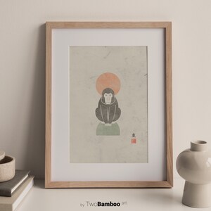 May include: A framed print of a black and white illustration of a monkey sitting on a green rock with a red sun behind it. The print has a red stamp with the Japanese character for "monkey" in the lower right corner.