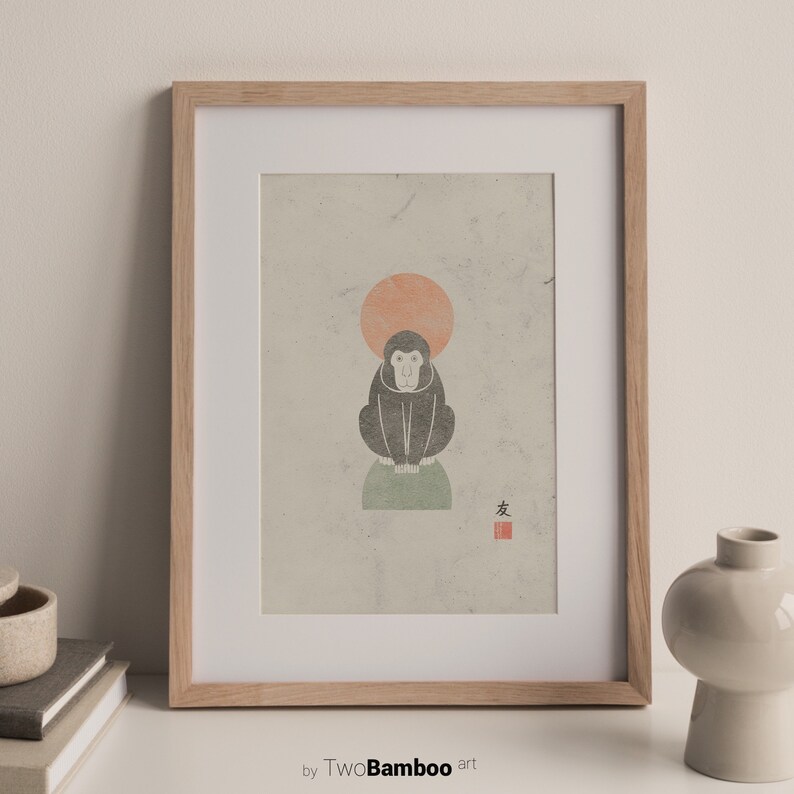 May include: A framed print of a black and white illustration of a monkey sitting on a green rock with a red sun behind it. The print has a red stamp with the Japanese character for "monkey" in the lower right corner.