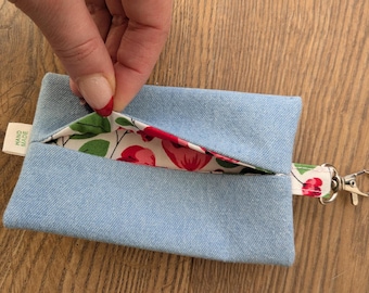 May include: A light blue denim card holder with a floral interior lining. The interior fabric features red and pink flowers with green leaves on a white background. A small tag reads "HAND MADE". A silver-coloured clasp is attached to a floral strap.