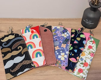 May include: Nine colorful fabric pouches with zipper closures and attached key rings. The pouches feature various patterns, including rainbows, flowers, and geometric designs.