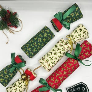 Puede incluir: Seis crackers de Navidad con patrones de acebo verde, rojo y blanco. Los crackers están atados con cintas verdes y rojas. Un pequeño letrero dice "Feliz Navidad".