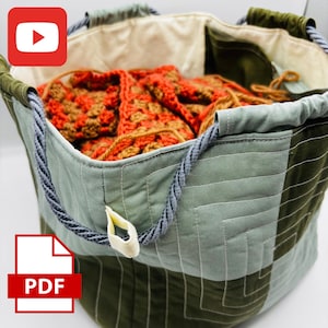 May include: A green, brown, and blue quilted storage bag with rope handles. The bag is filled with orange and brown crocheted squares.