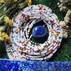 May include: A white beaded waist chain with colorful beads, including red, orange, yellow, green, blue, and purple. The chain is wrapped around a blue lapis lazuli stone.