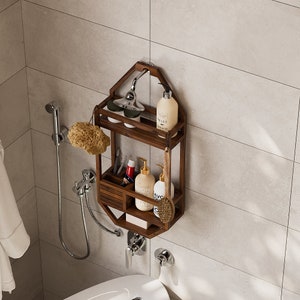 Puede incluir: Estante de ducha de madera marr&oacute;n oscuro con dos niveles y un caj&oacute;n peque&ntilde;o. El estante est&aacute; montado en una pared alicatada y contiene varios art&iacute;culos de tocador, incluyendo botellas de jab&oacute;n y una esponja vegetal. Tambi&eacute;n se ven un cabezal de ducha y un grifo.