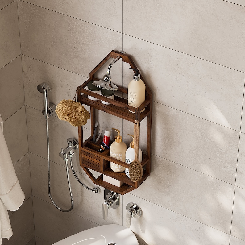Puede incluir: Estante de ducha de madera marr&oacute;n oscuro con dos niveles y un caj&oacute;n peque&ntilde;o. El estante est&aacute; montado en una pared alicatada y contiene varios art&iacute;culos de tocador, incluyendo botellas de jab&oacute;n y una esponja vegetal. Tambi&eacute;n se ven un cabezal de ducha y un grifo.