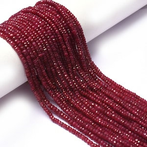 Könnte beinhalten: Eine Strähne tief roter Rubinperlen, jede Perle ist facettiert und hat eine leicht unregelmäßige Form. Die Perlen sind auf einem dünnen Faden aufgefädelt und bereit für die Schmuckherstellung.