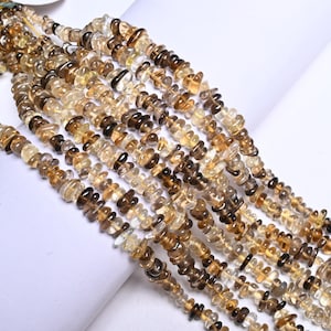 May include: Strands of natural citrine chip beads in varying shades of yellow and brown. The beads are irregular in shape and size, strung together to create a textured appearance. The gemstones are displayed against a white background.