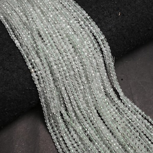 May include: Strands of small, faceted, pale green beads. The beads are strung together, creating a flowing, textured appearance. The beads are displayed against a dark background, highlighting their color and shine. Ideal for jewelry making.
