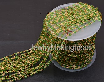 May include: A spool of gold-plated chain with green glass beads. The chain is wound around a white spool.