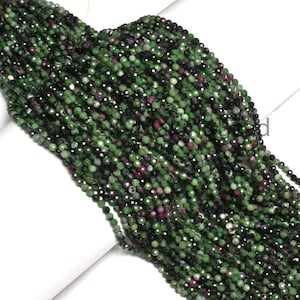 Puede incluir: Un largo hilo de pequeñas cuentas redondas facetadas con un patrón moteado de verde bosque profundo, negro y rosa magenta vibrante. Las cuentas están ensartadas en una línea densa y continua, mostrando una superficie reflectante y multicolor.