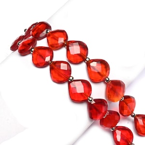 Pode incluir: Um close-up de um colar com contas vermelhas quadradas facetadas. As contas são enfiadas com pequenos conectores prateados. O colar é exibido em uma superfície branca, destacando a cor e o design vibrantes.