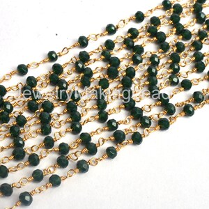 Könnte beinhalten: Eine Strähne aus dunkelgrünen, facettierten Glasperlen, die auf einer goldenen Kette aufgefädelt sind. Die Perlen sind gleichmäßig verteilt und die Kette ist zart.