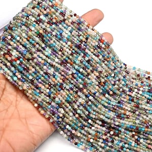 May include: A collection of multi-coloured gemstone beads. The beads are small, round, and faceted, with a variety of colours including blue, green, red, purple, and peach. The beads are strung together, creating a flowing, textured appearance.