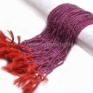 May include: Strands of small, faceted, deep pink beads cascade from a white surface, with a vibrant red tassel on the left. The beads are tightly strung, creating a luxurious texture. The image is well-lit, highlighting the beads' sparkle.
