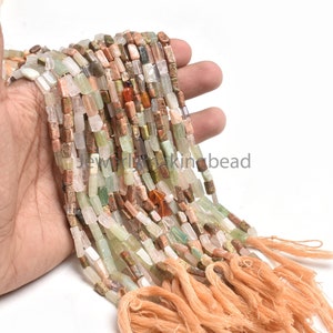 Puede incluir: Una hebra de cuentas de piedras preciosas multicolores, con tonos de verde, marrón, rosa y blanco. Las cuentas son rectangulares y tienen un acabado pulido. La hebra está acabada con un borla.