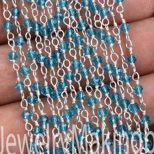 May include: A strand of silver chain with blue faceted beads. The chain is made of small, delicate links and the beads are evenly spaced.