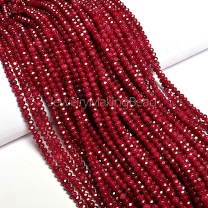 Può includere: Primo piano di più fili di perline sfaccettate rosso intenso. Le perline sono piccole e di dimensioni uniformi, con una forma leggermente irregolare. Le perline sono infilate insieme, creando un aspetto fluido e strutturato. Le perline sono di un ricco colore rosso scuro.