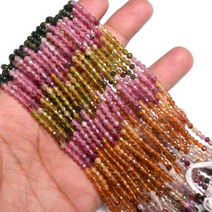 Puede incluir: Una hebra de cuentas de turmalina multicolores. Las cuentas son facetadas y tienen una variedad de colores, incluyendo verde, rosa y naranja. Las cuentas están enhebradas en un hilo blanco.