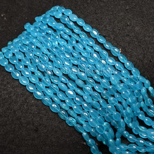 May include: Strands of light blue oval-shaped beads. The beads are strung together, creating a flowing, textured appearance. The beads have a translucent quality, and the color is a bright, clear blue. Ideal for jewelry making.