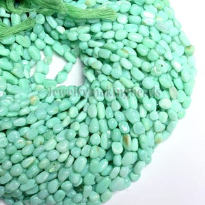 Könnte beinhalten: Nahaufnahme eines Haufens hellgrüner, oval geformter Perlen. Die Perlen sind glatt und haben eine leicht glänzende Oberfläche. Oben ist ein Bündel hellgrüner Schnur zu sehen. Der Text "Jewelrymakingbeads" ist teilweise sichtbar.